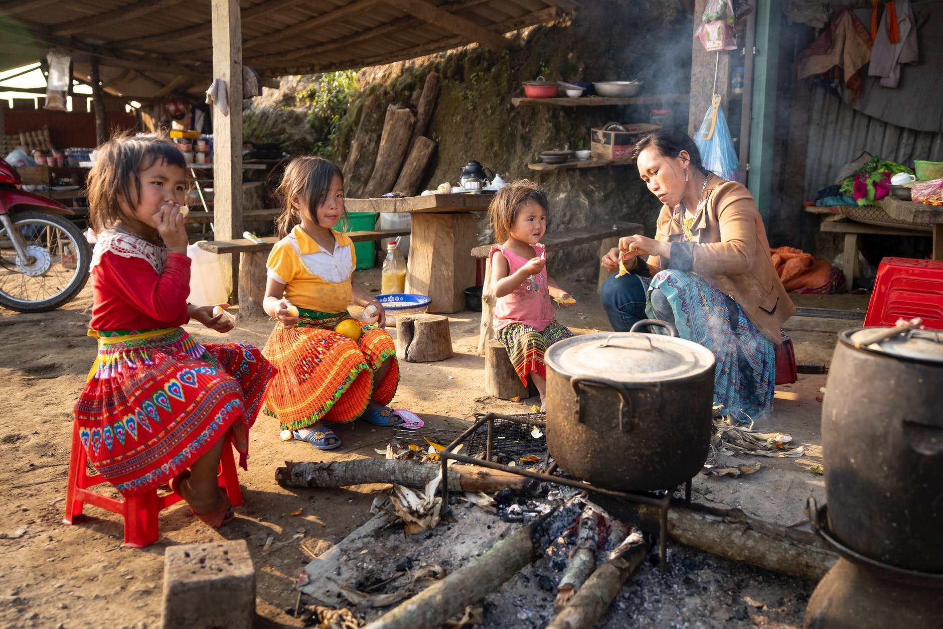 asian mother and girls sitting near campfire in indigenous village